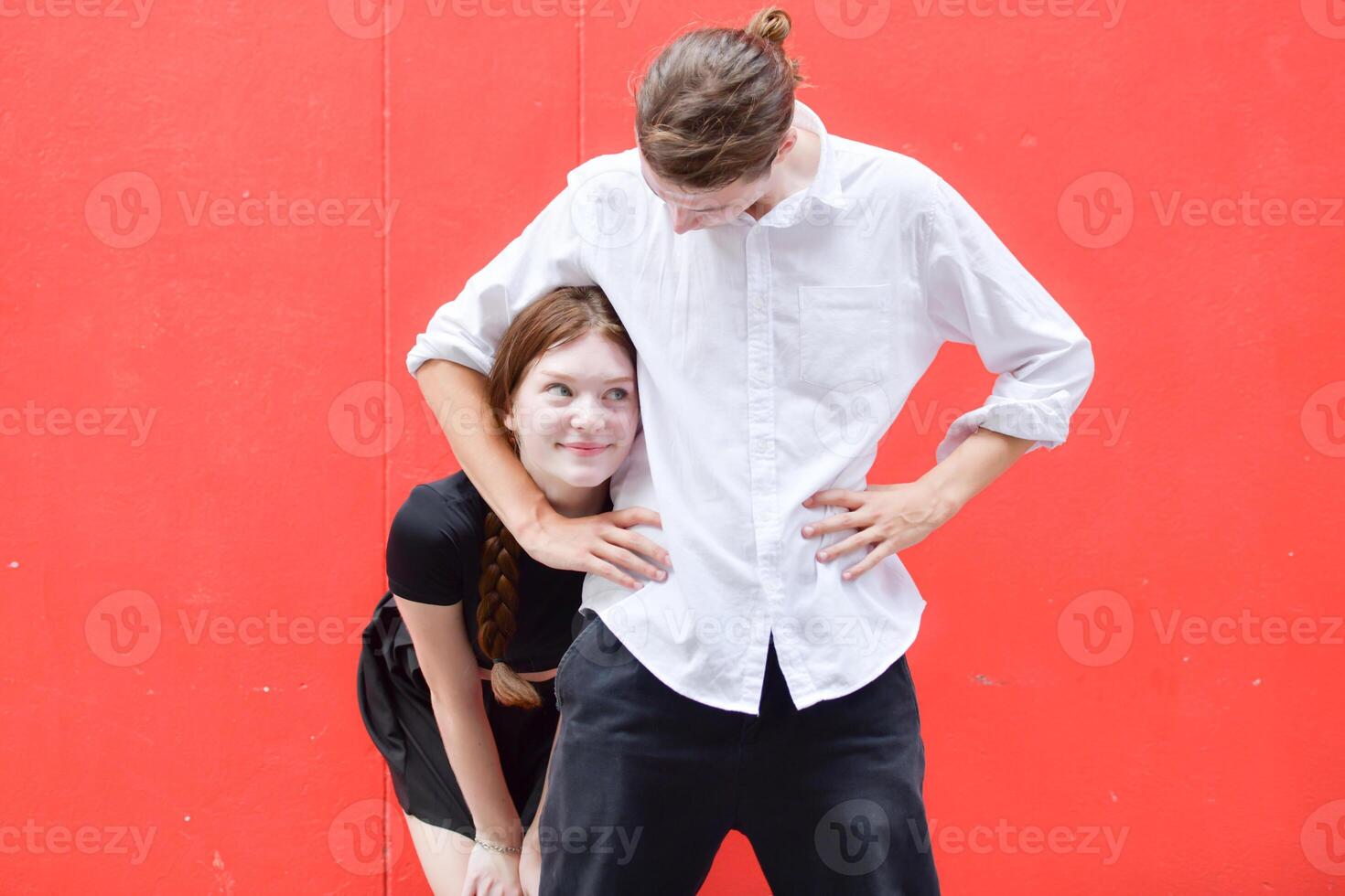 un Pareja es disfrutando un verano vacaciones en el rojo pared fondo, felizmente demostración su amor a cada otro. foto