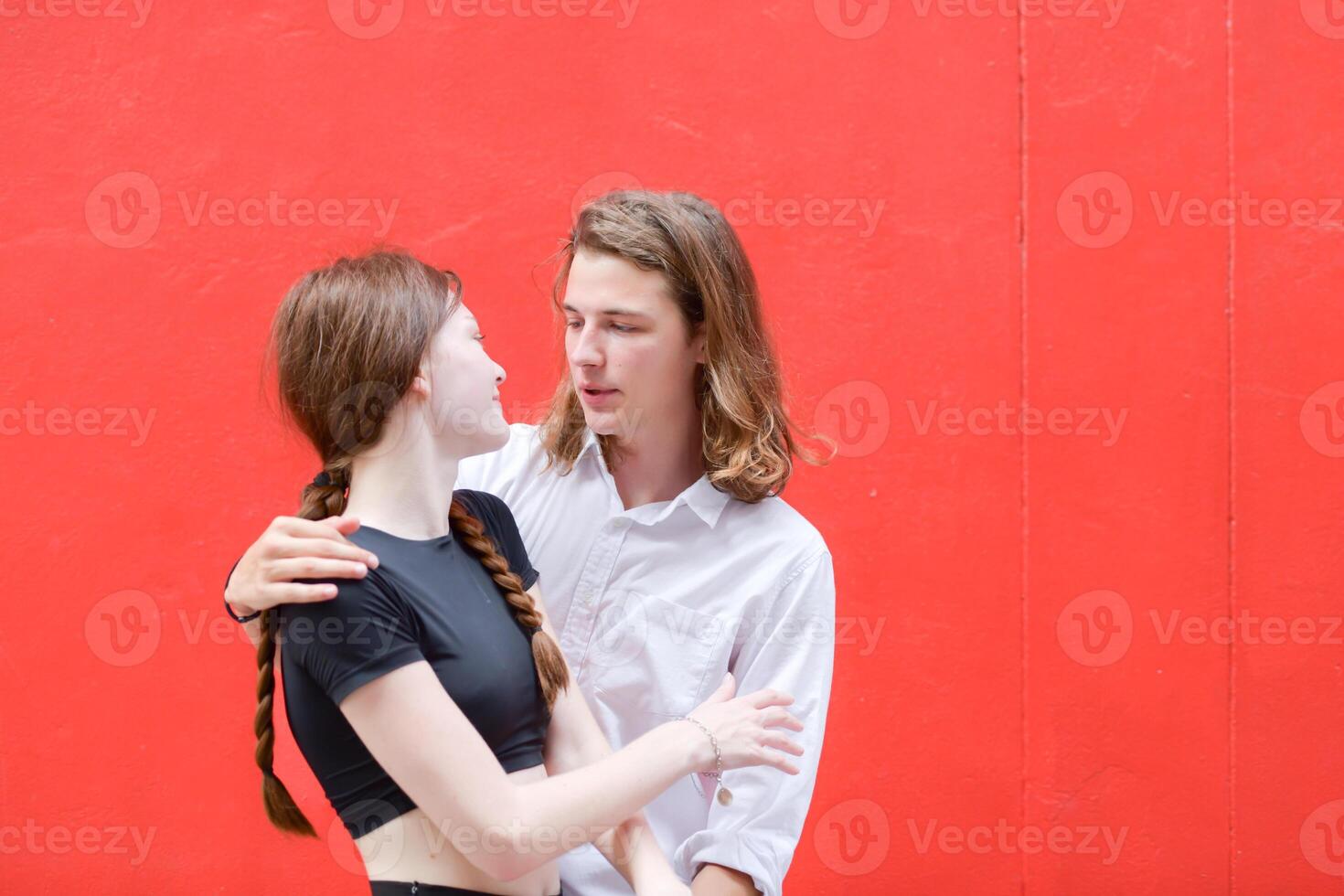 A couple is enjoying a summer vacation in the red wall background, happily showing their love to each other. photo