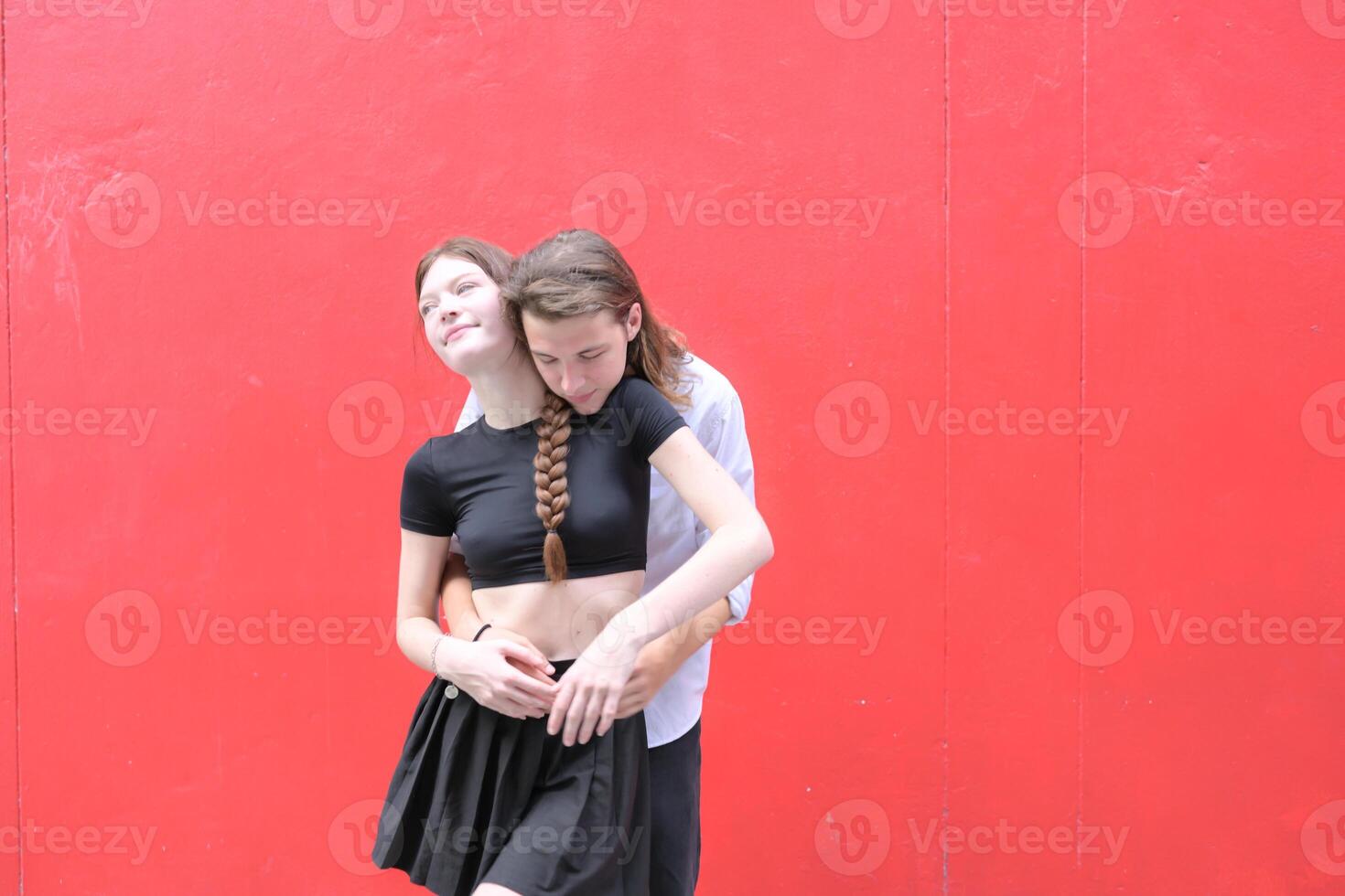 A couple is enjoying a summer vacation in the red wall background, happily showing their love to each other. photo