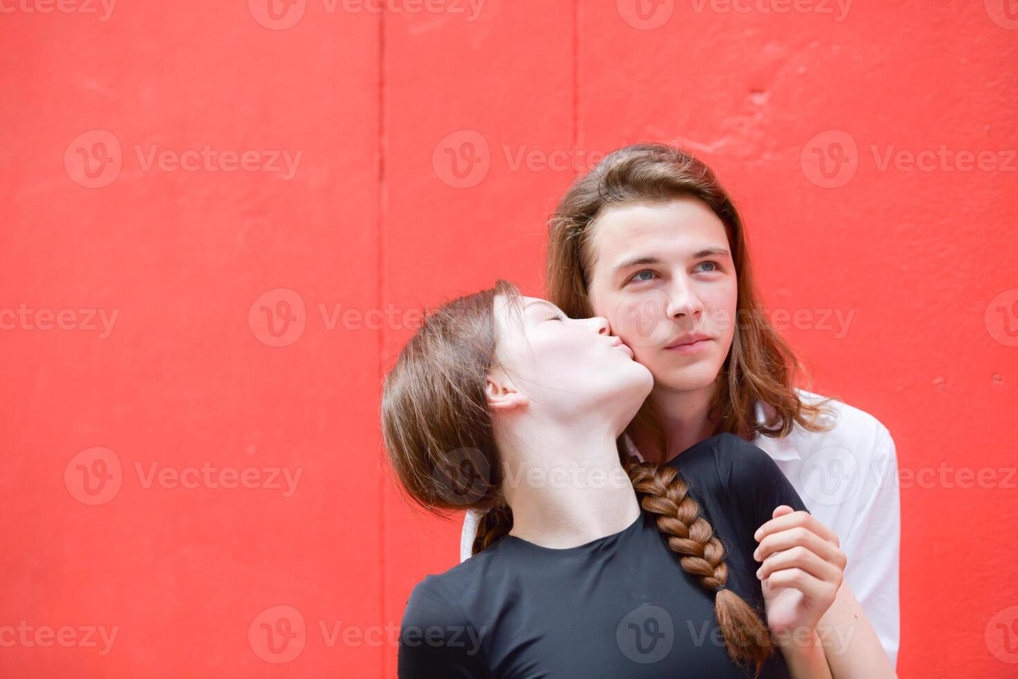 A couple is enjoying a summer vacation in the red wall background, happily showing their love to each other. photo