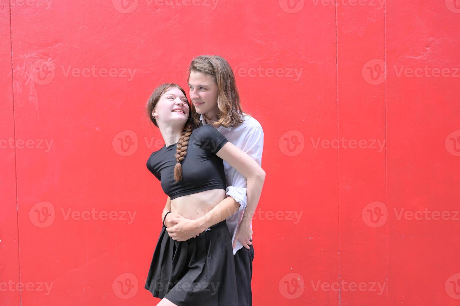 A couple is enjoying a summer vacation in the red wall background, happily showing their love to each other. photo