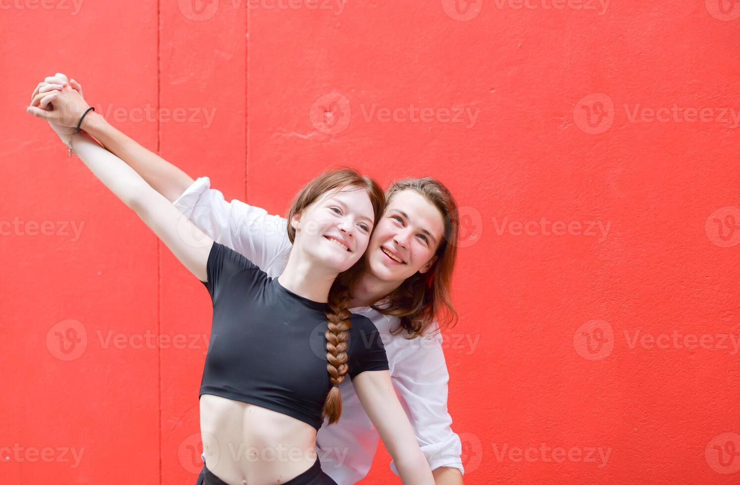 A couple is enjoying a summer vacation in the red wall background, happily showing their love to each other. photo
