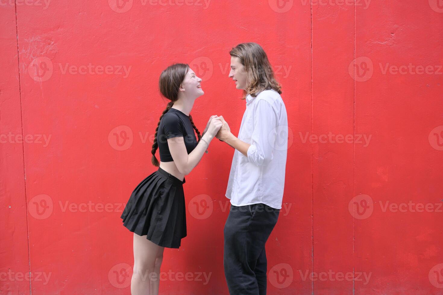 A couple is enjoying a summer vacation in the red wall background, happily showing their love to each other. photo