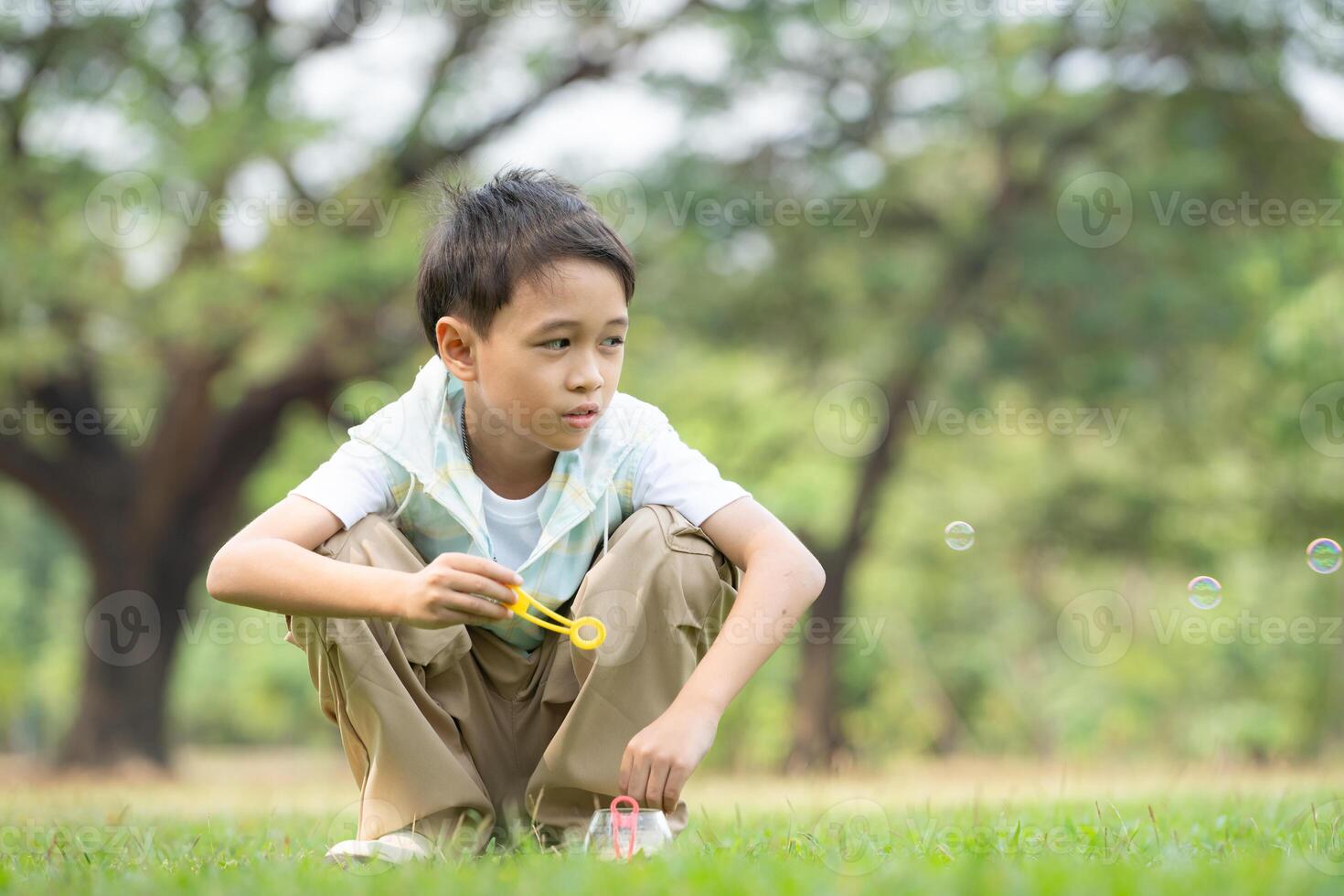 Boy sitting in the park with blowing air bubble, Surrounded by greenery and nature photo