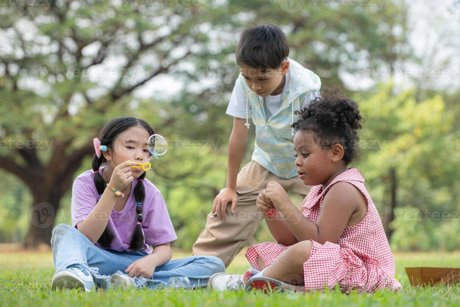 Children sitting in the park with blowing air bubble, Surrounded by greenery and nature photo