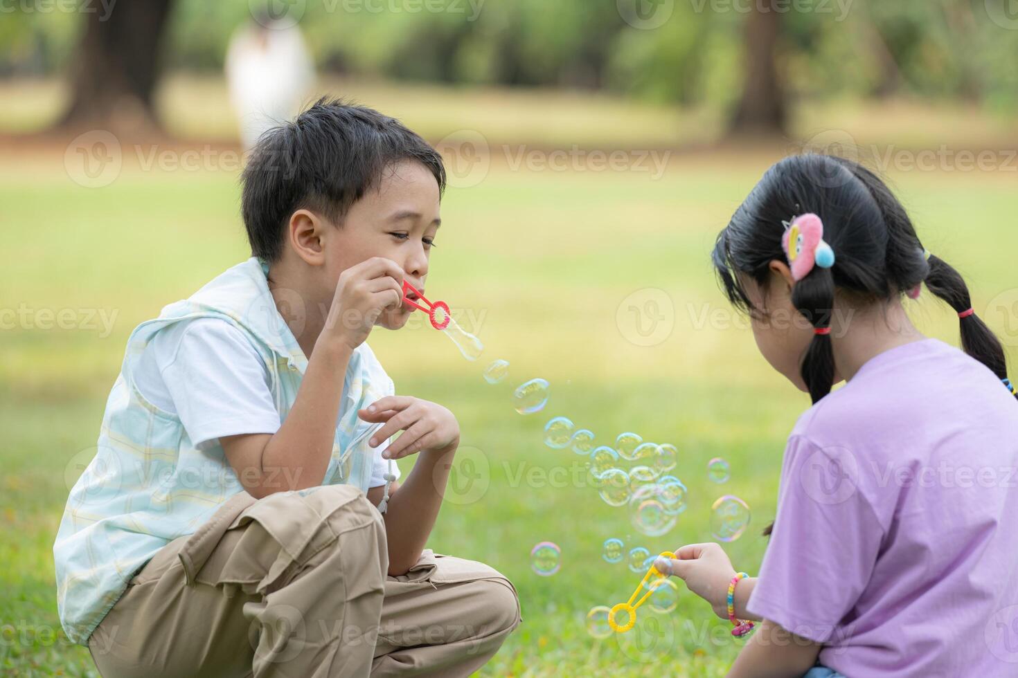 Children sitting in the park with blowing air bubble, Surrounded by greenery and nature photo