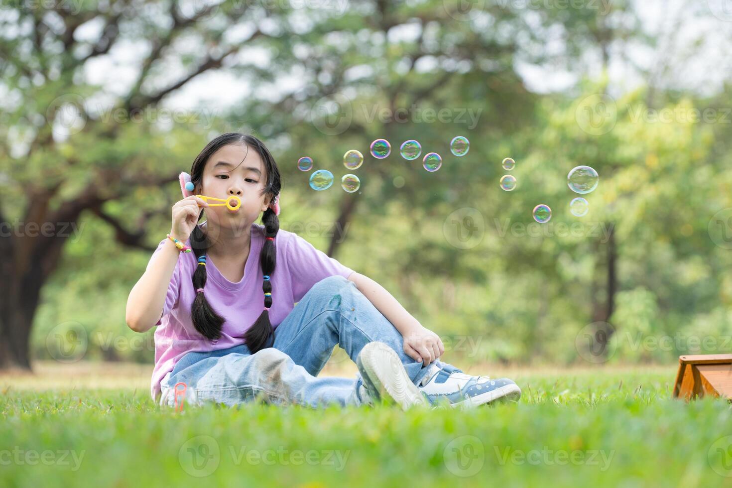 niña sentado en el parque con soplo aire burbuja, rodeado por verdor y naturaleza foto