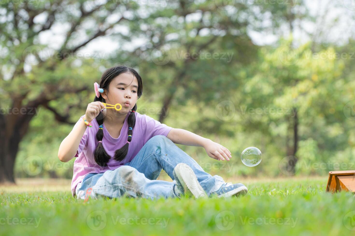 Girl sitting in the park with blowing air bubble, Surrounded by greenery and nature photo