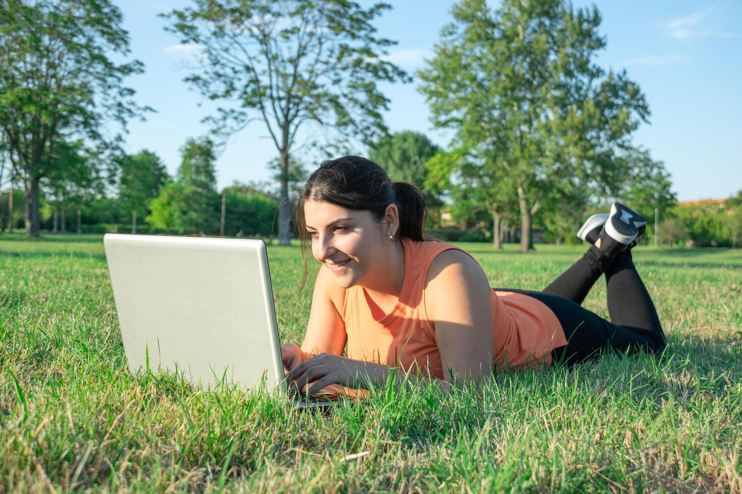 joven caucásico mujer acostado en parque utilizando su ordenador portátil muy contento foto