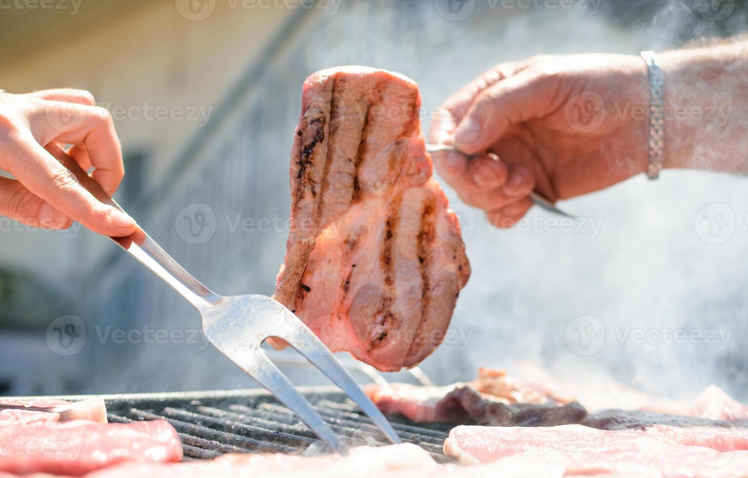 Hand holding steak cooking on smoking barbecue on terrace. photo
