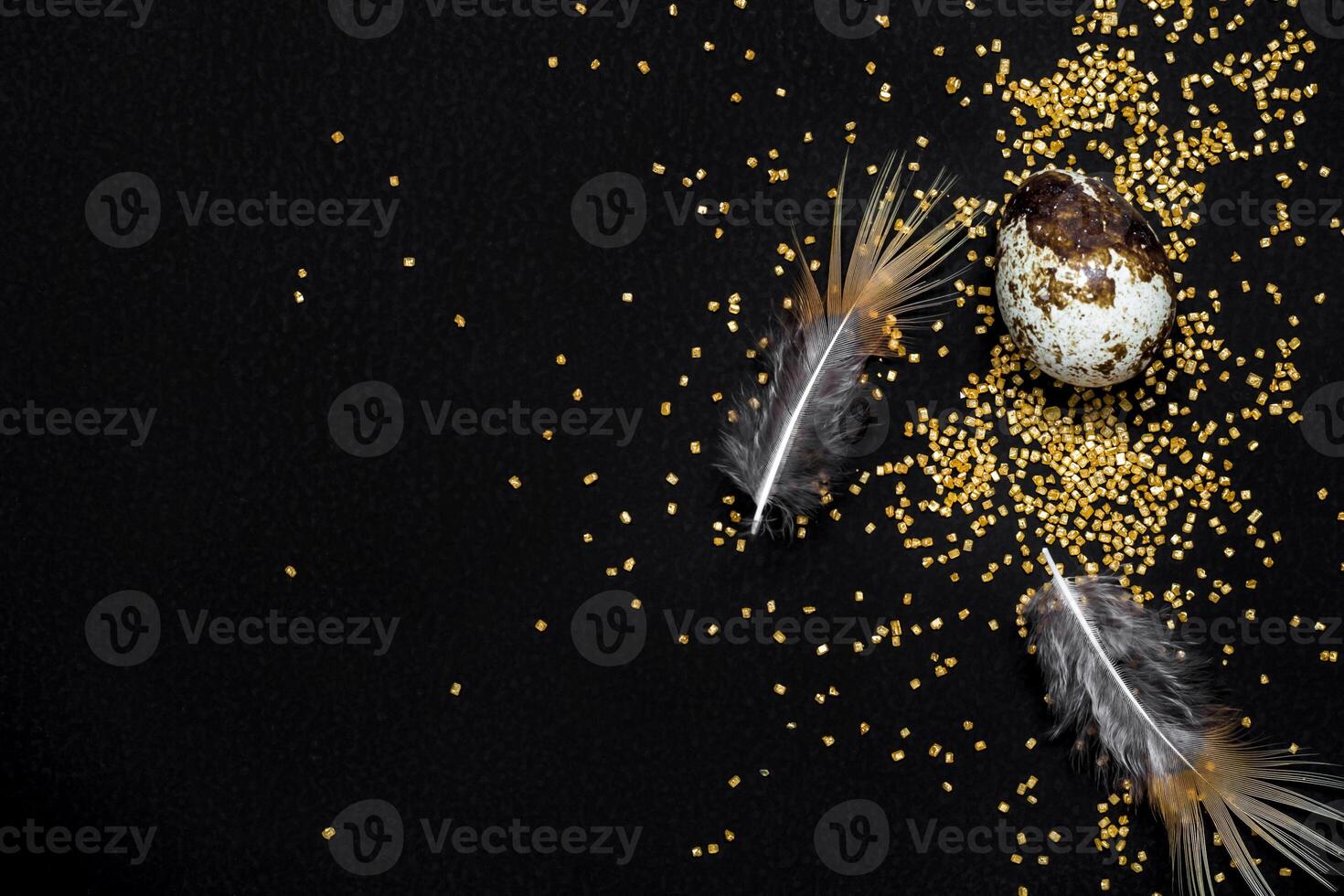 Moody easter background. Quail eggs, feathers and golden sugar sprinkles on black background. Happy easter photo