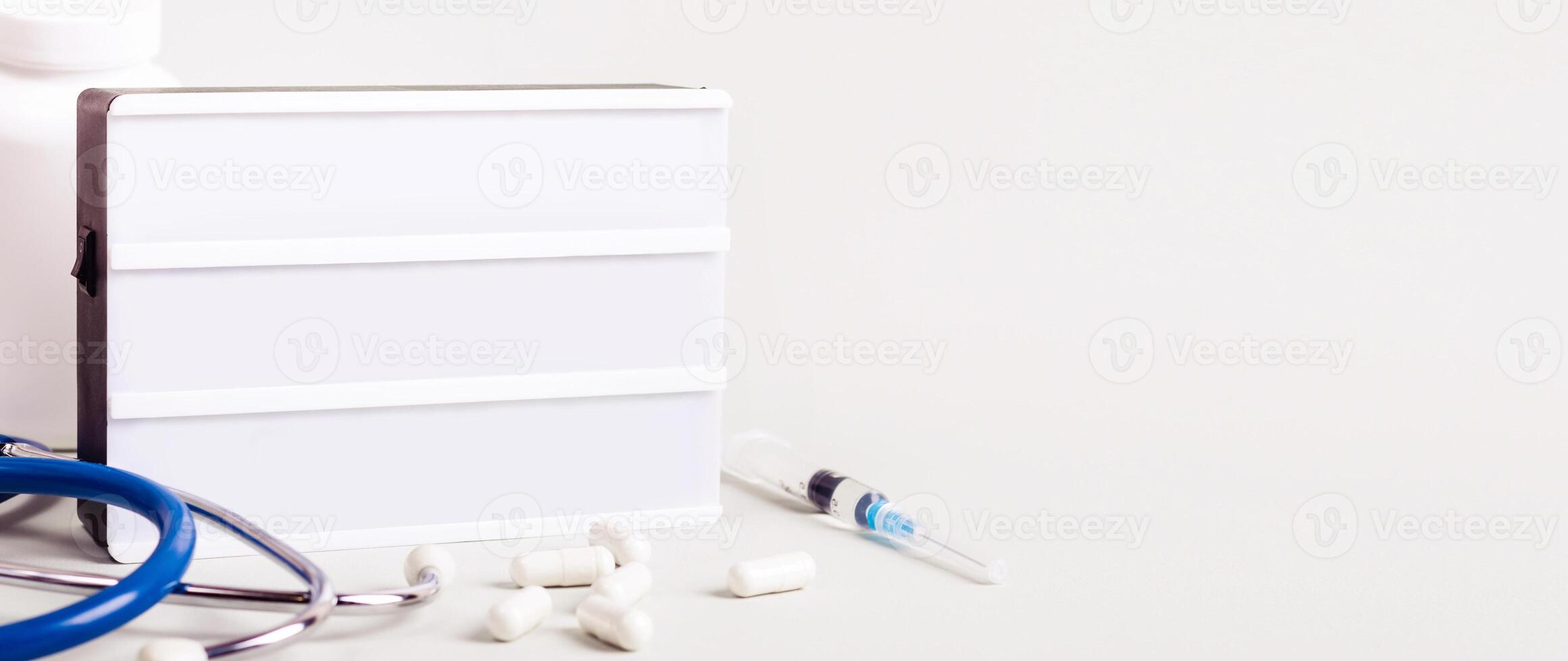 Medicine treatment concept. Empty Lightboard, stethoscope, pills and syringes. Banner format. photo