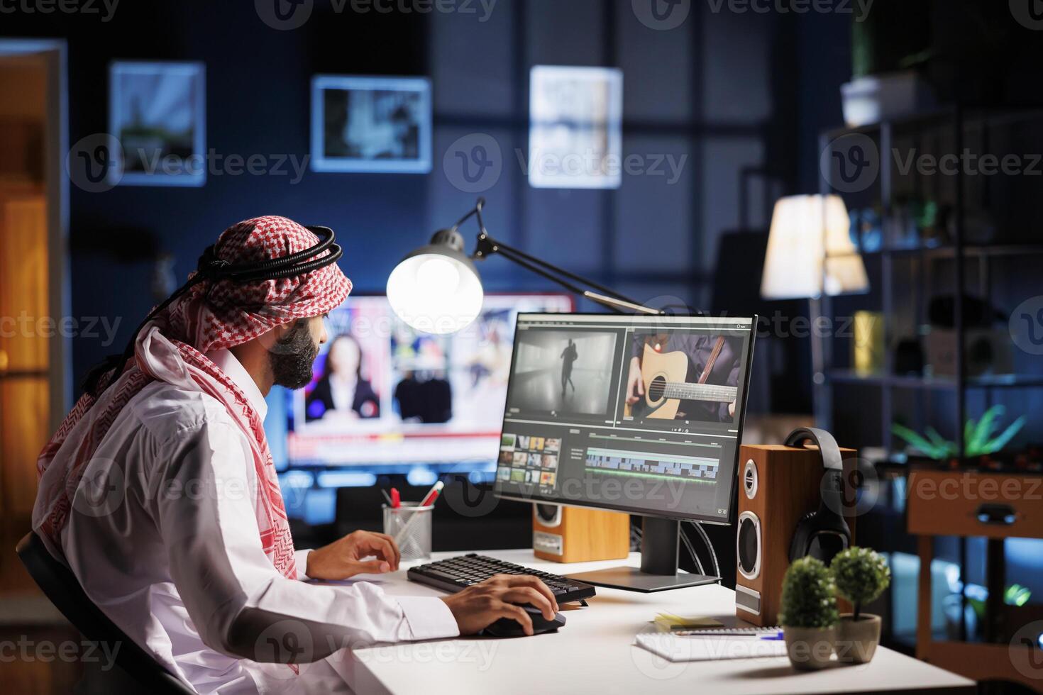 A Middle Eastern man edits video information on his computer screen using multimedia software. Arab guy director works on a movie montage cut on a computer monitor in this side-view image. photo