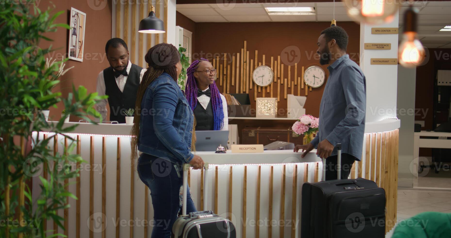 Receptionist greeting tourists at hotel, asking for personal information to verify online room booking. Couple on vacation travelling with trolley bags, arriving at front desk reception. photo