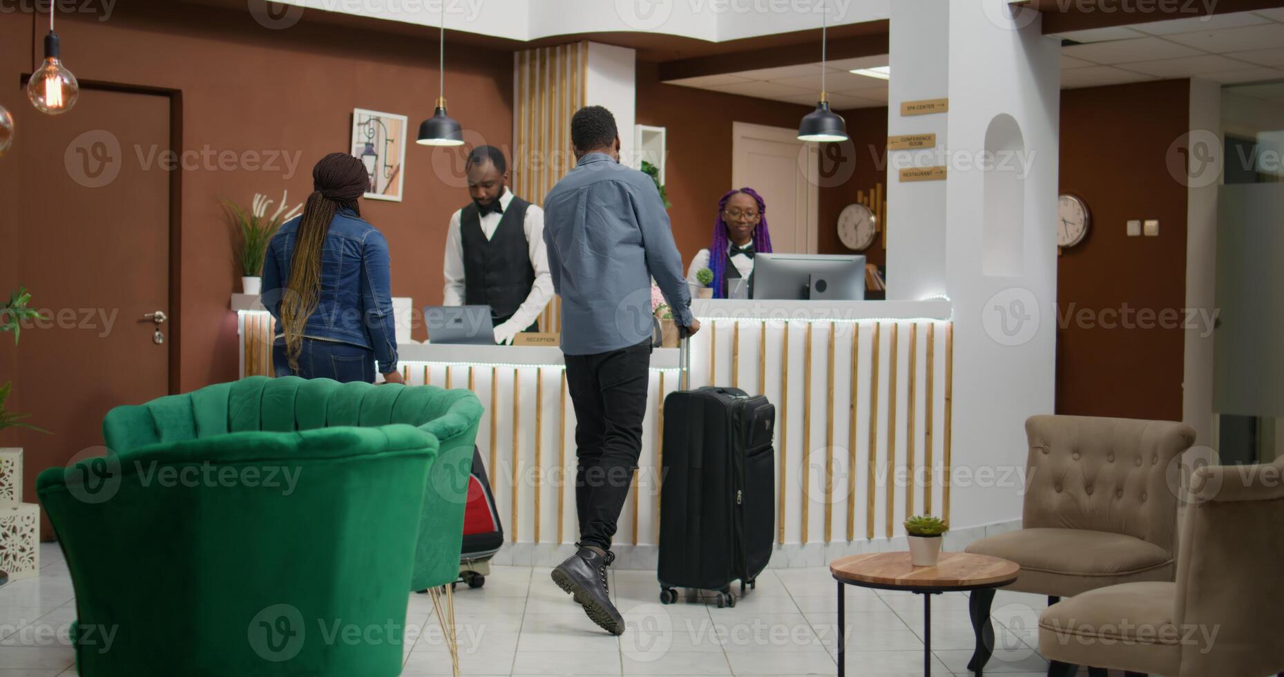 africano americano personas llegar a hotel, hablando a personal miembros acerca de habitación reserva y cheque en procedimiento. hombre y mujer llegando en vestíbulo con carretilla bolsas, Luna de miel viaje. foto