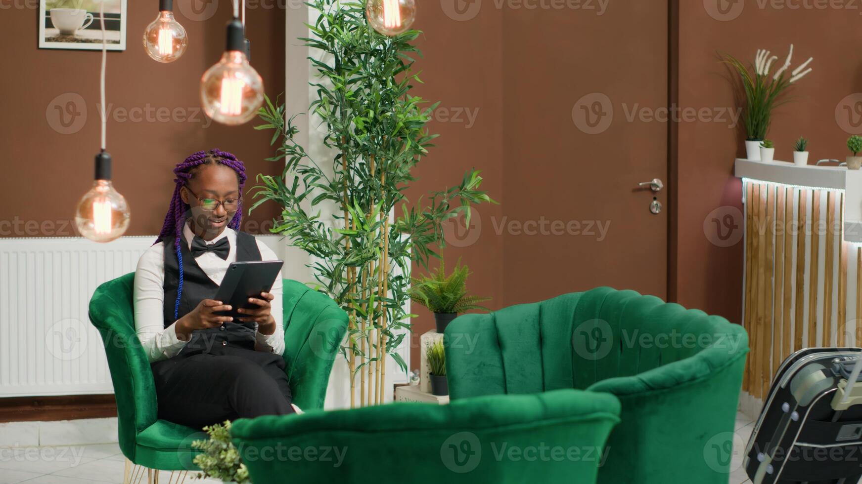 African american staff checking reservations on tablet, ensuring excellent concierge service to guests. Woman lodging manager keeping track of online bookings using digital device. photo