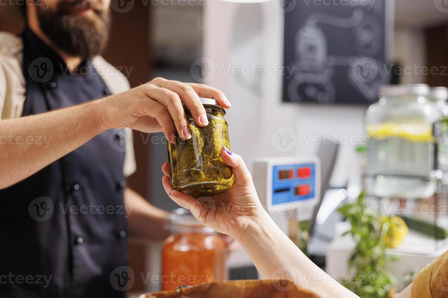Close up shot of customer at checkout counter in zero waste shop, buying locally sourced ecofriendly vegetables from storekeeper. Client purchasing pickles jar in local neighborhood store photo