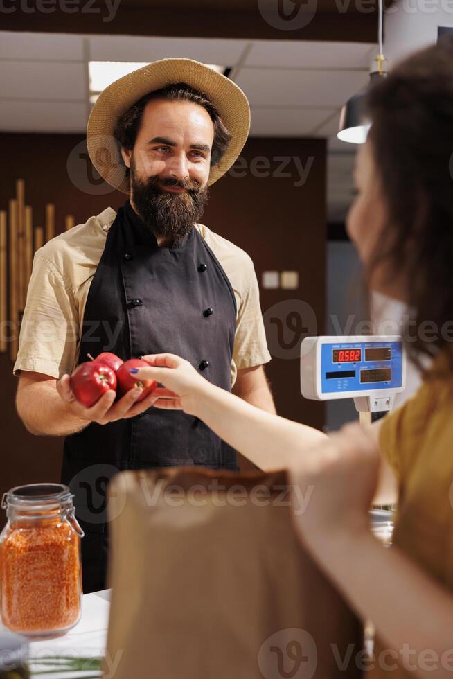 Customer at zero waste store checkout counter paying for additives free vegetables. Client in plastic free local grocery shop using decomposable paper bag for low carbon dioxide emissions photo