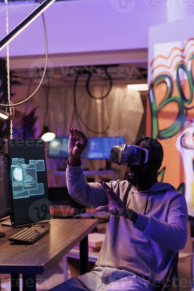 Hacker wearing vr helmet doing illegal activities and breaching online security systems in metaverse. African american man using virtual reality headset while cracking password photo