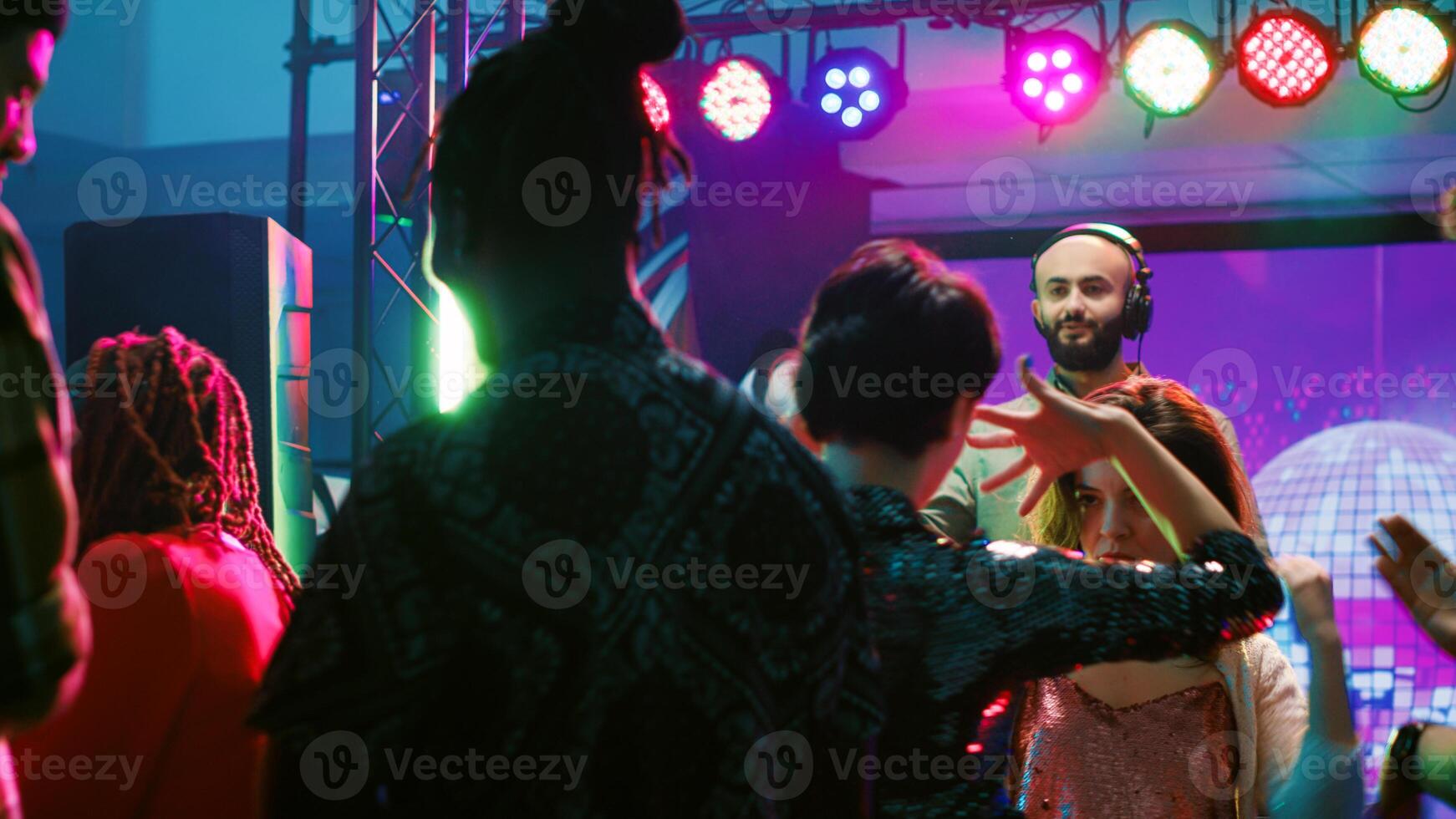 miedoso mujer hablando en danza piso a club, bailando y molesto a tener conversacion mientras DJ mezclas electrónico música. alegre joven amigos teniendo divertido a Club nocturno con multitud de gente. foto