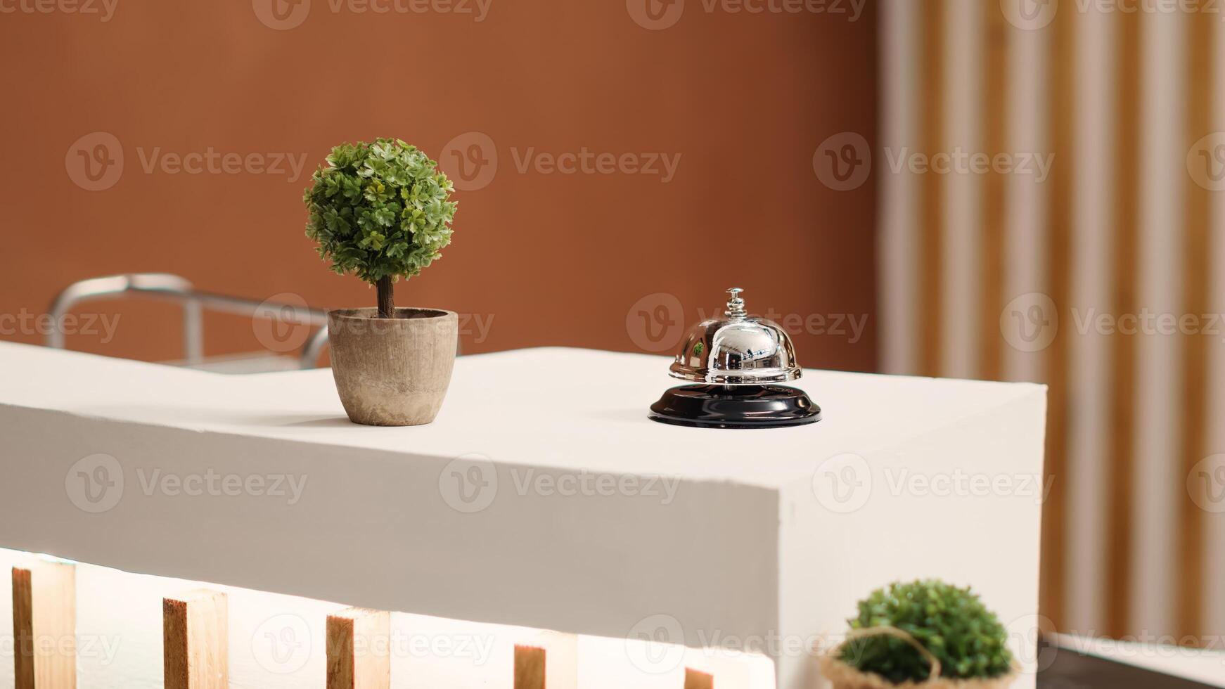 Elegant concierge bell on modern stylish hotel lobby check in desk. Reception bell next to mini plant on empty warm hospitality industry lounge reception counter, close up photo