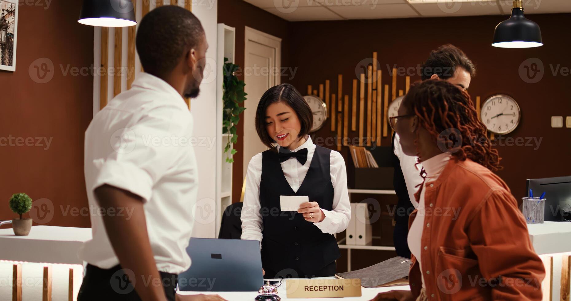 Tourists handing over room access key to friendly asian receptionist at front desk. Happy guests checking out from hotel after nice stay while concierge employee communicates feedback to manager photo