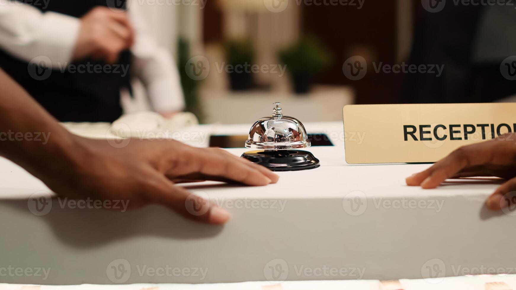 Close up of african american guests ringing concierge bell at reception counter during check in process. Vacation trip tourists ready to book in their reservation at hotel lounge front desk photo