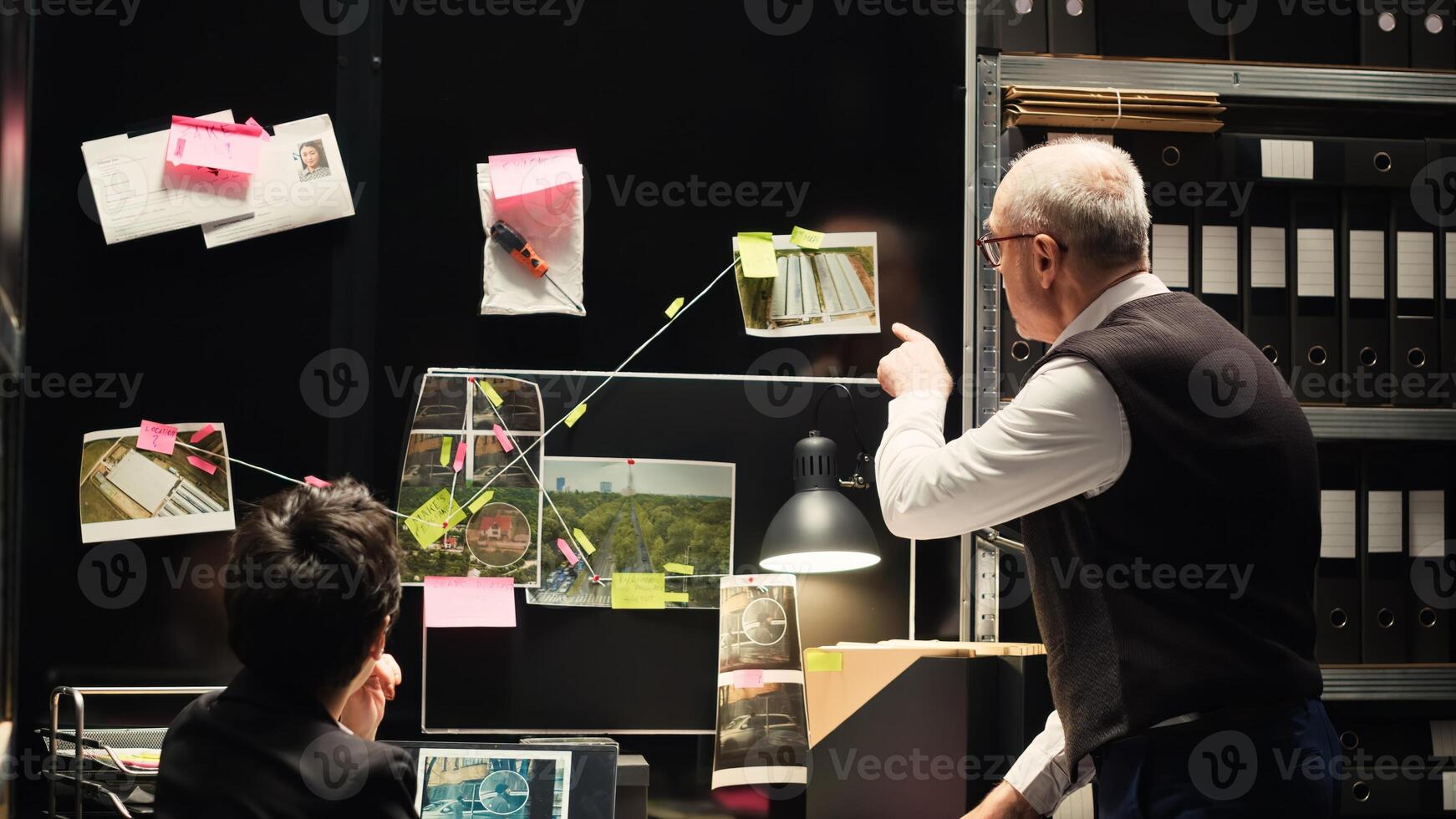 Two investigators review evidence and incriminating proof to find suspect, searching for his identity on surveillance photos. Forensic experts analyzing handwriting and fingerprints. photo