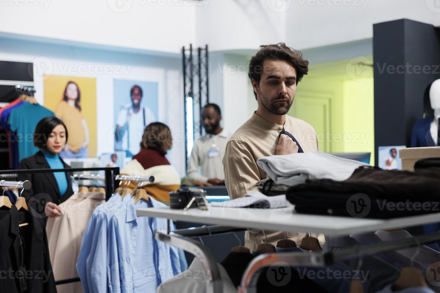 Clothing store client selecting menswear and accessory while choosing wardrobe outfit. Young caucasian man searching for tie and shirt while shopping in department mall boutique photo