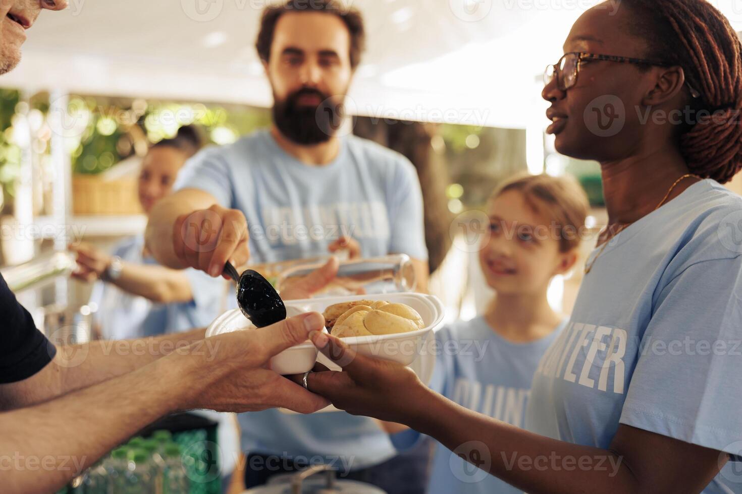 Friendly volunteers supporting the less fortunate by offering humanitarian aid through food distribution. Young people combating poverty by participating at outdoor hunger relief food drive program. photo