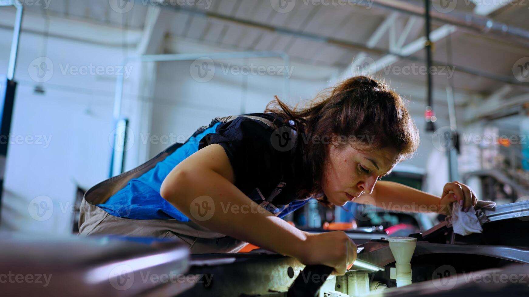 POV shot of meticulous engineer opening car hood in repair shop, using work light to check for damages during routine maintenance. Garage worker using professional tool to look inside automobile photo