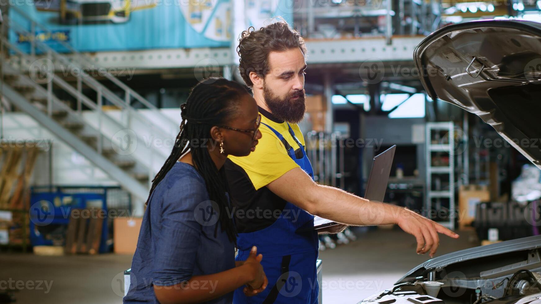 Serviceman in repair shop using laptop to calculate repairments invoice for client after fixing malfunctions found inside car. Expert using device to determine final costs after mending vehicle photo