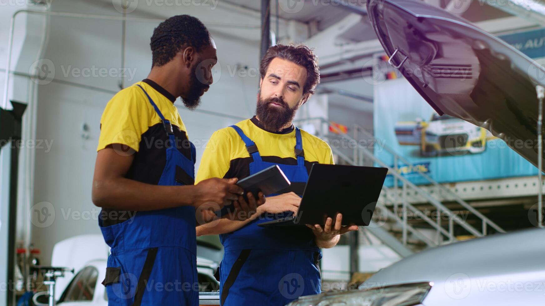 Mechanics in car service ordering new parts for damaged vehicle using laptop and tablet. Coworkers looking online for components to replace old ones in malfunctioning automobile photo