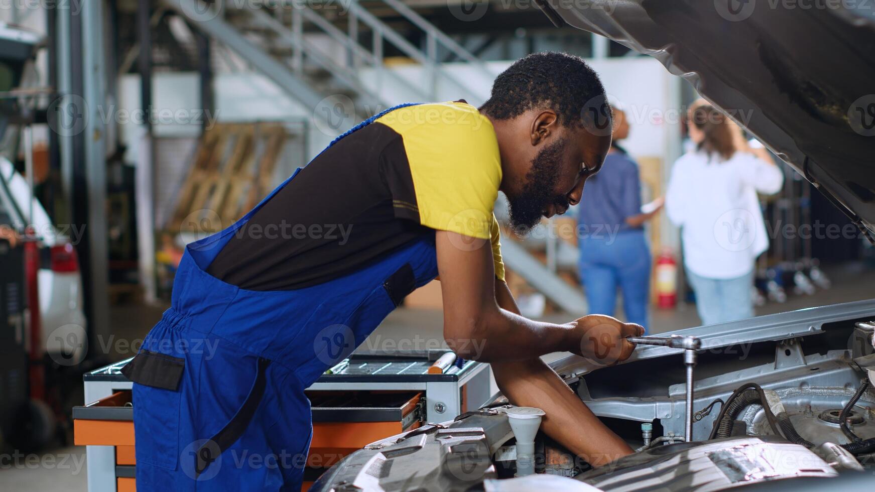 Trained engineer in car service uses torque wrench to tighten bolts inside vehicle after fixing components inside. African american repair shop expert utilizes professional tools to mend automobile photo