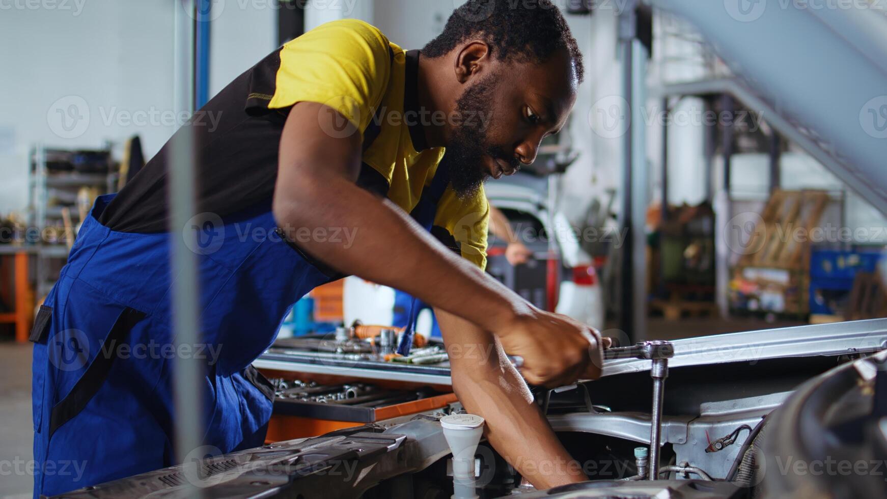 Knowledgeable employee in auto repair shop using virtual reality glasses to visualize car components in order to fix them. Professional wearing modern vr headset while working on broken vehicle photo