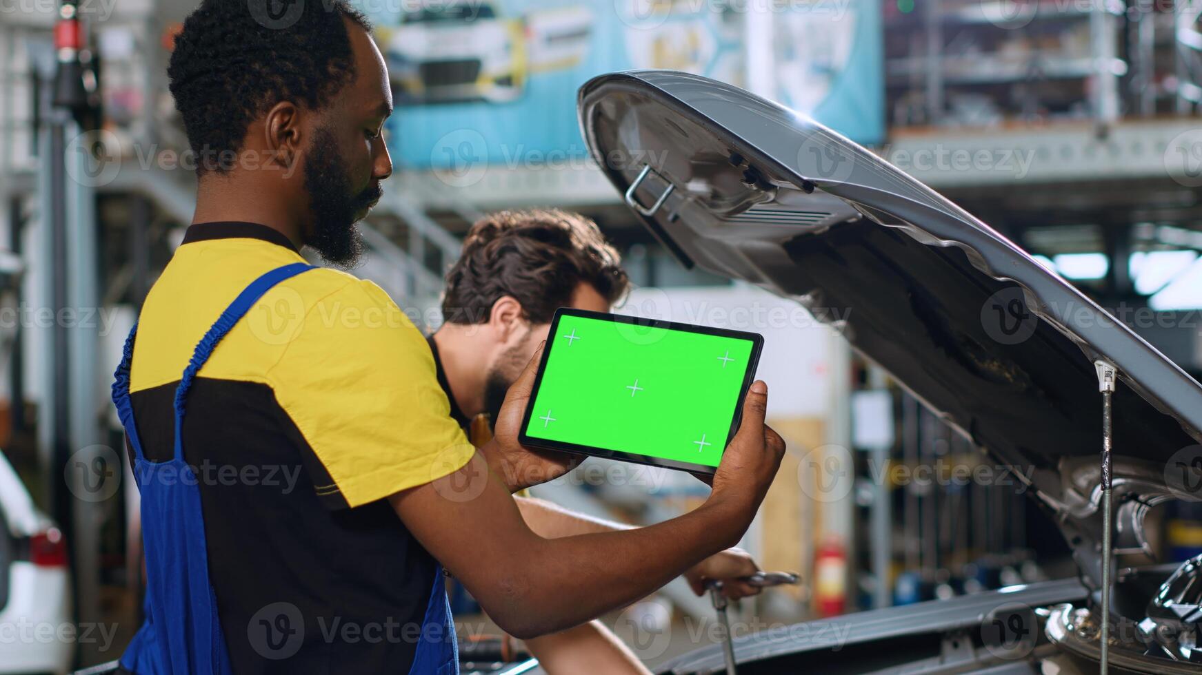 Mechanic using green screen tablet in car service to watch tutorial on how to fix unknown problem. Employee using chroma key device to look online for video showing how to repair broken vehicle part photo