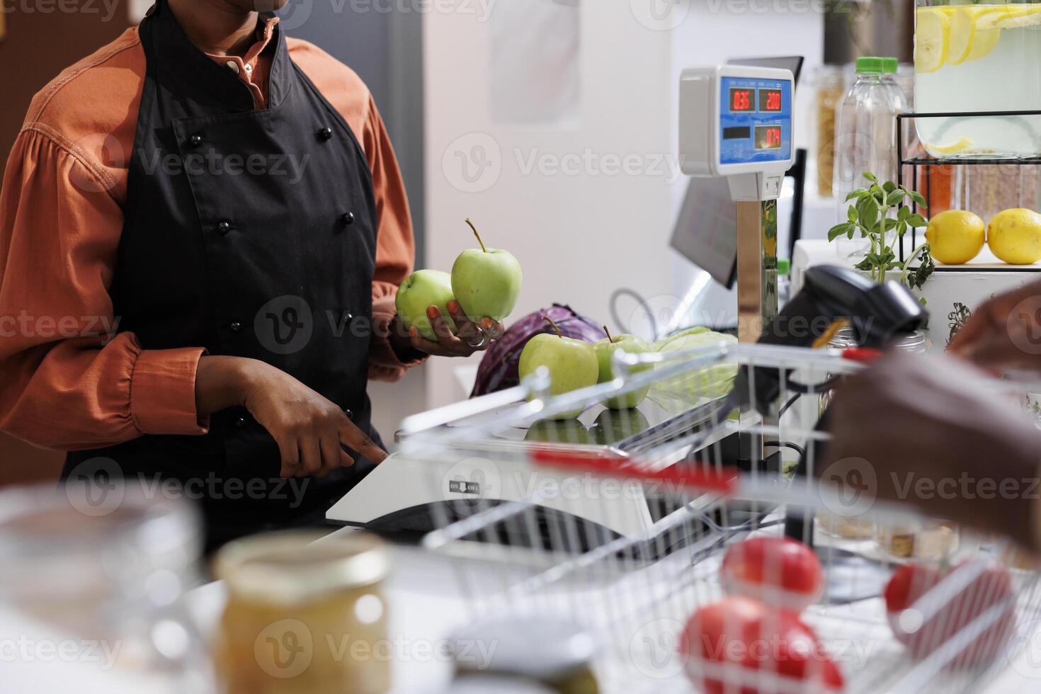 selectivo atención en africano americano hembra vendedor participación verde manzanas y peso un repollo en un escala. clientes lata comprar un variedad de sano elementos, incluso frutas y vegetales. foto