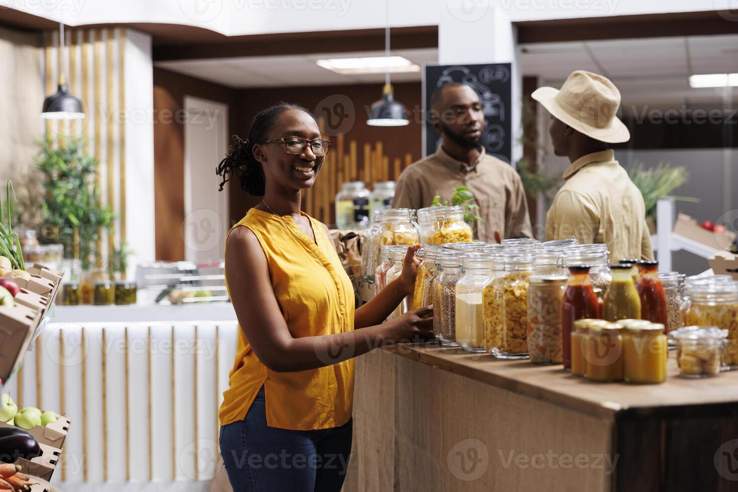 Female customer smiles as she looks at the camera. Sustainable products in reusable containers, wooden shelves. Diverse range of local goods, bulk items. Professional and customer-friendly service. photo