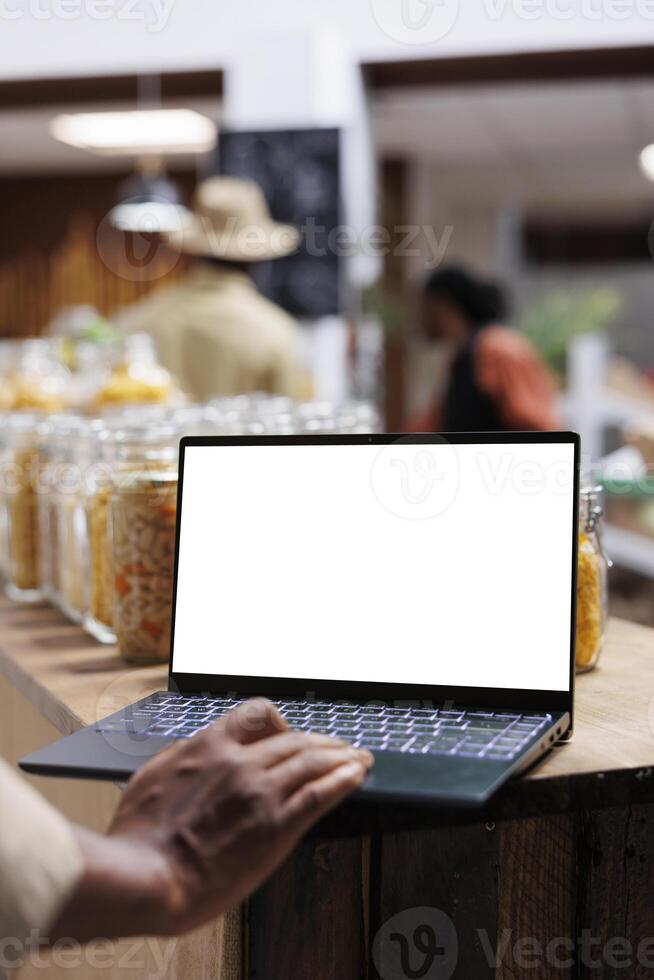 Detailed view of a digital laptop showing an isolated copyspace mockup template in an eco friendly supermarket. Close-up of african american person using minicomputer with blank white screen display. photo