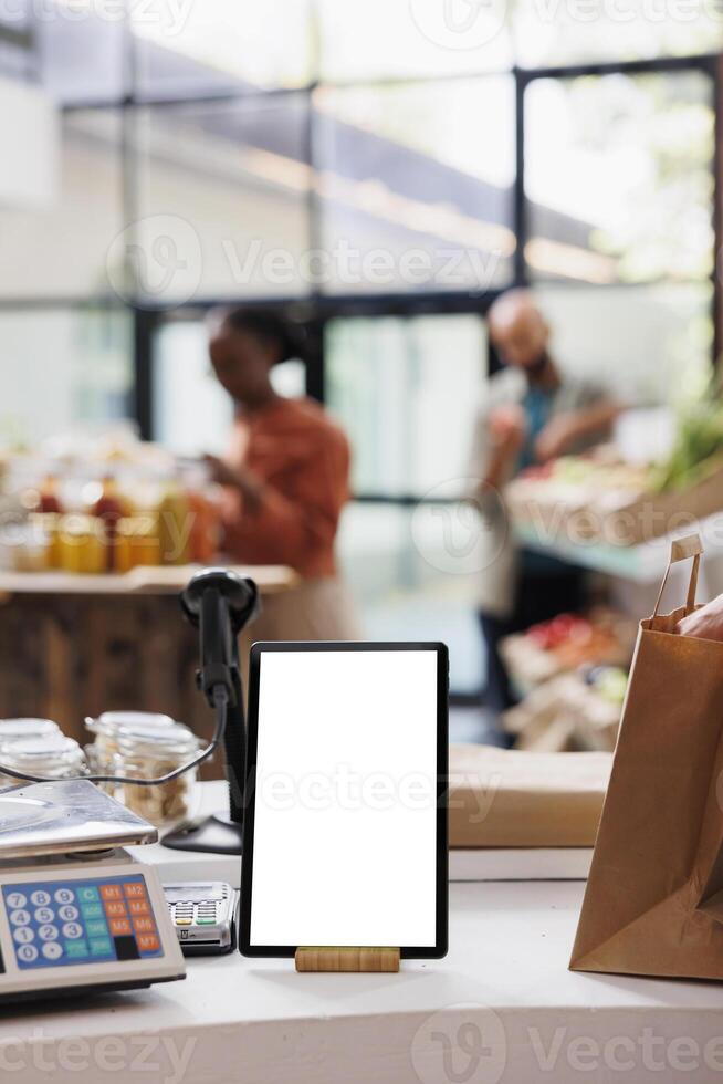 A digital tablet with a blank chromakey mockup template is vertically positioned near glass jars in this image. Smart device with an isolated white screen sits on the counter. photo