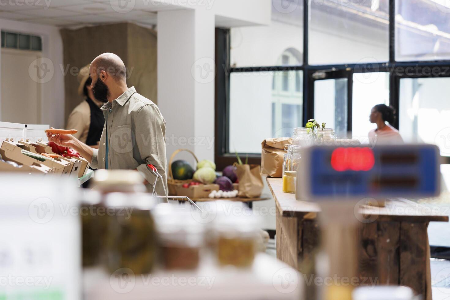 Arab man holding and looking at fresh carrot at vegetable stand. Middle eastern customer appears to be in an environmentally friendly store and looking to get food that will sustain healthy lifestyle. photo