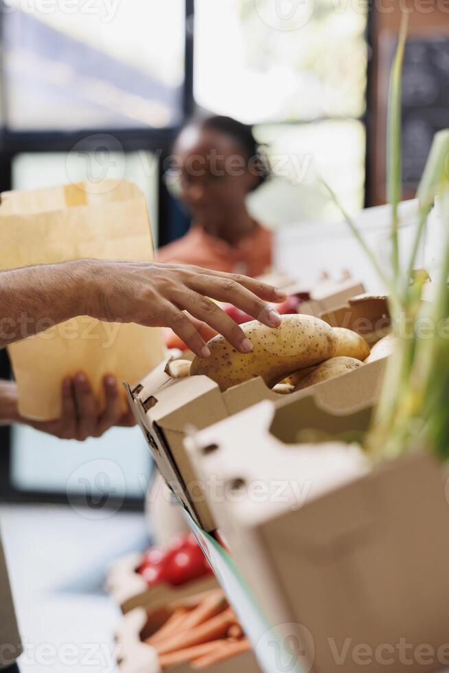 Close-up of a man selecting potatoes grown nearby from the eco-friendly store's shelf. Detailed photo of a customer choosing recently harvested produce to prepare a nutritious meal.