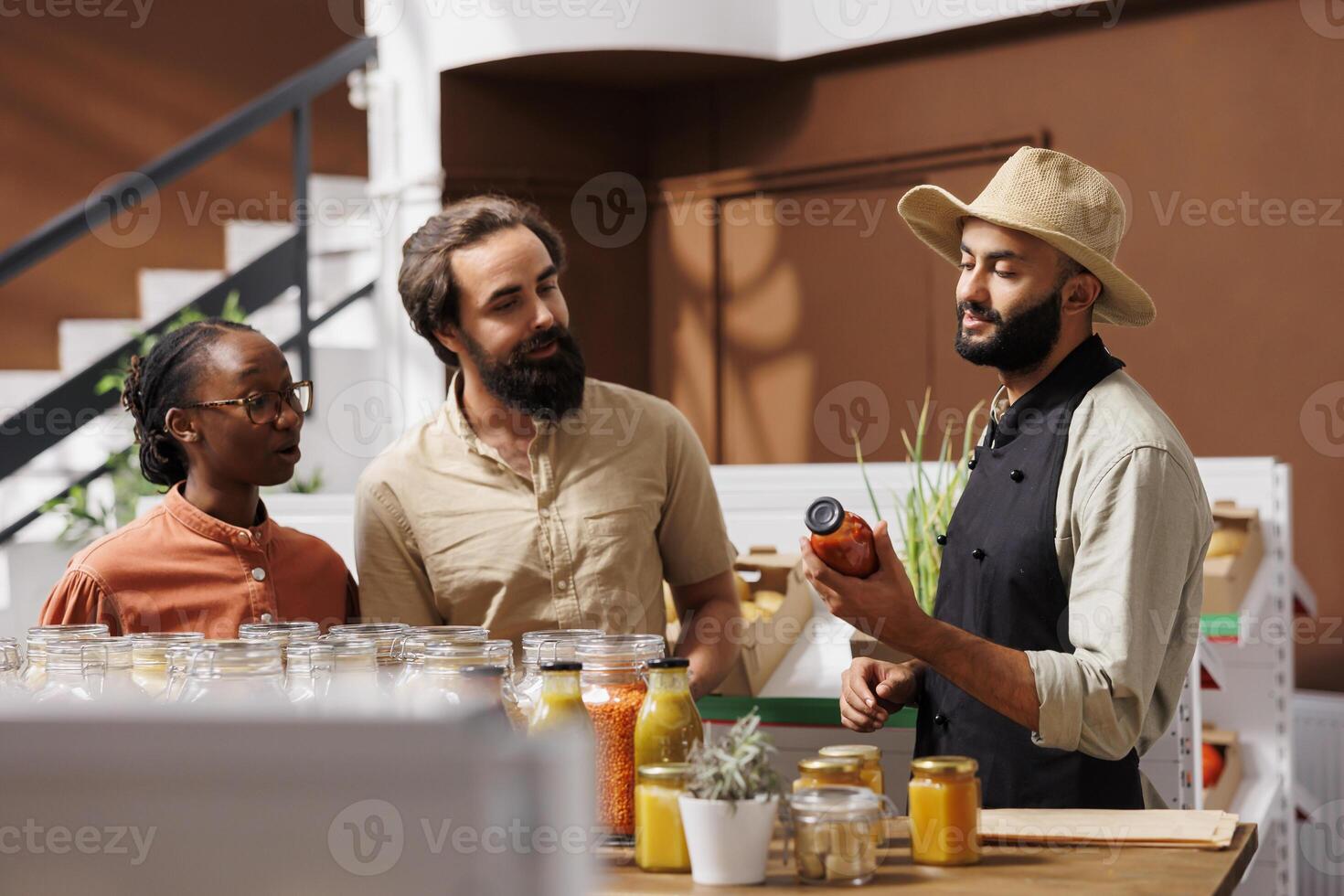 At organic supermarket, vendor suggests bio pantry products to young couple. Middle eastern shopkeeper sharing his family secret pasta bolognese recipe with multicultural customers. photo