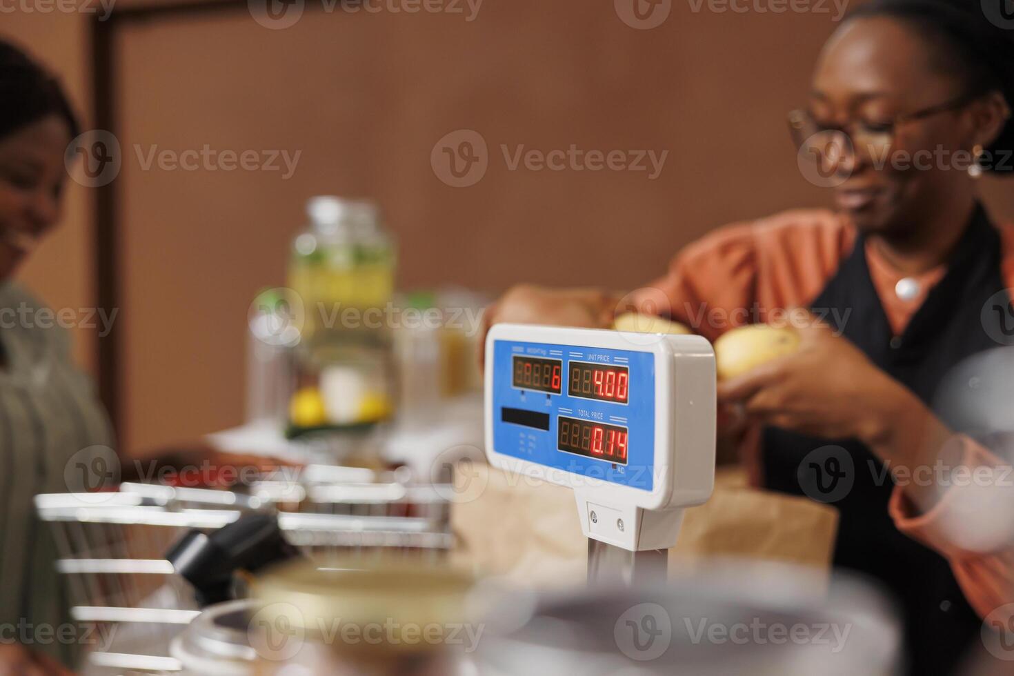 Black woman shopping at a grocery store with organic produce. The cashier assists customer at checkout counter using plastic free packaging for locally grown fruits and vegetables. photo