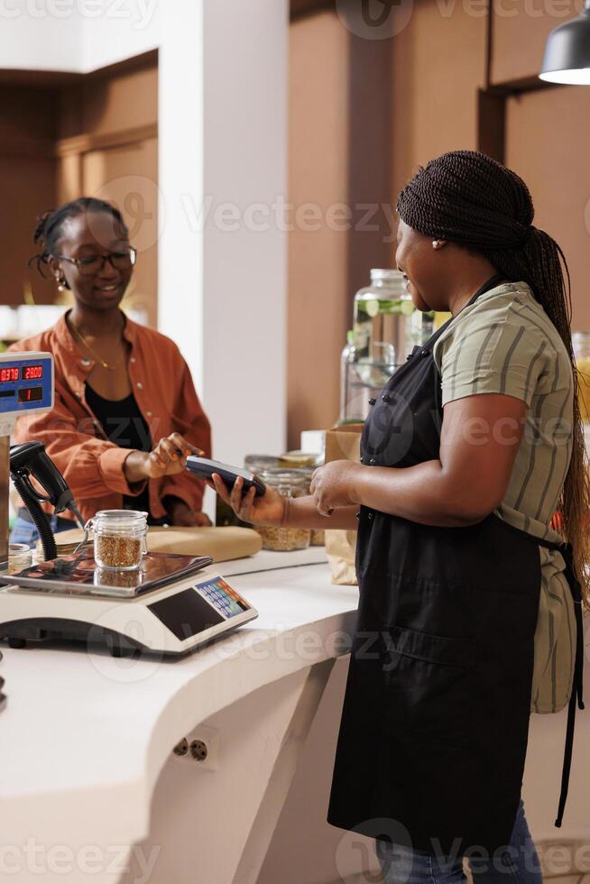 African American female client smiles while using her credit card for cashless payment. The local food market focuses on locally grown organic produce and eco friendly practices. photo