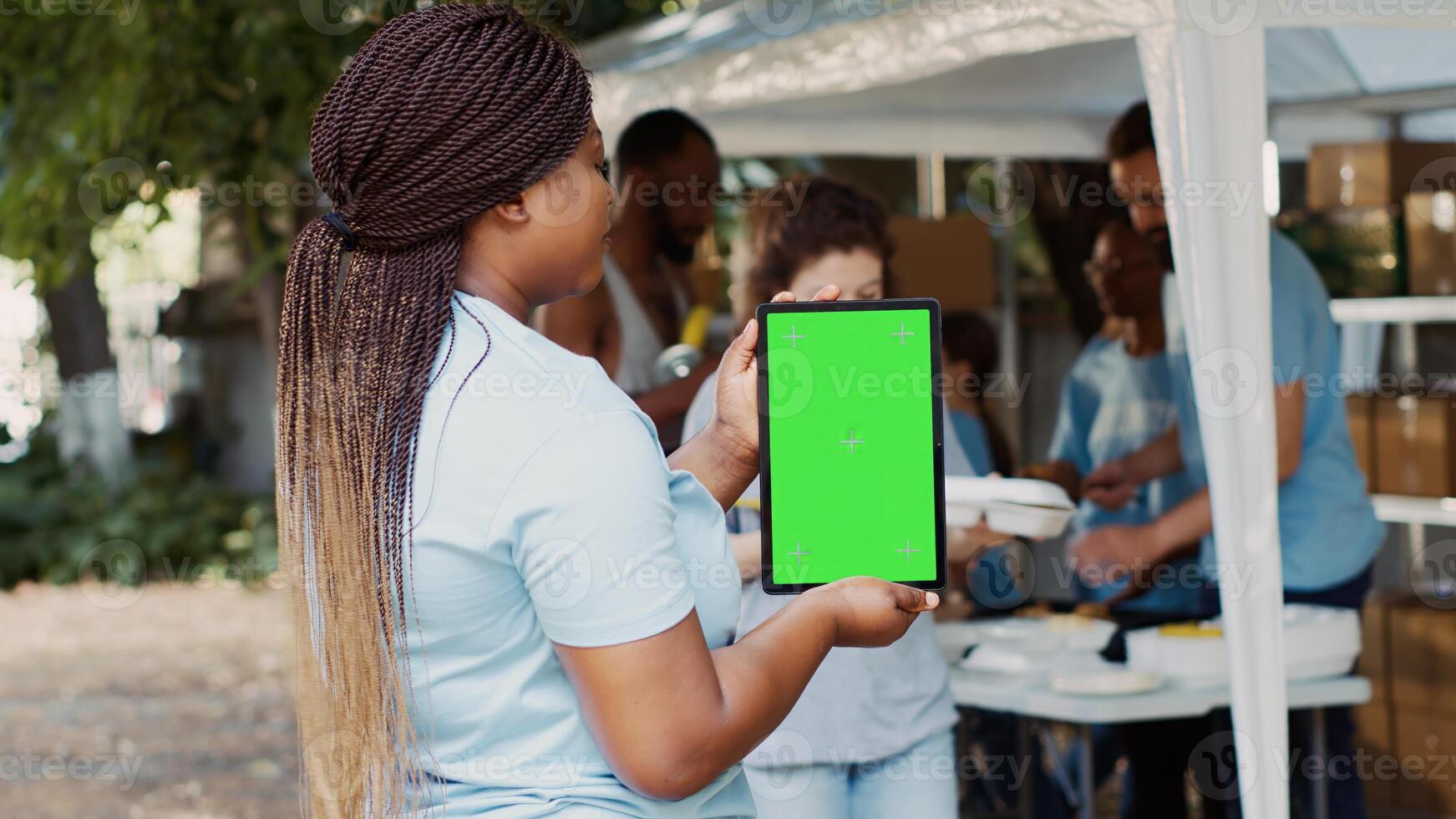 An isolated chromakey template for humanitarian messages on smart tablet is held by african american charity worker. Voluntary black woman grasping digital device with blank green screen display. photo