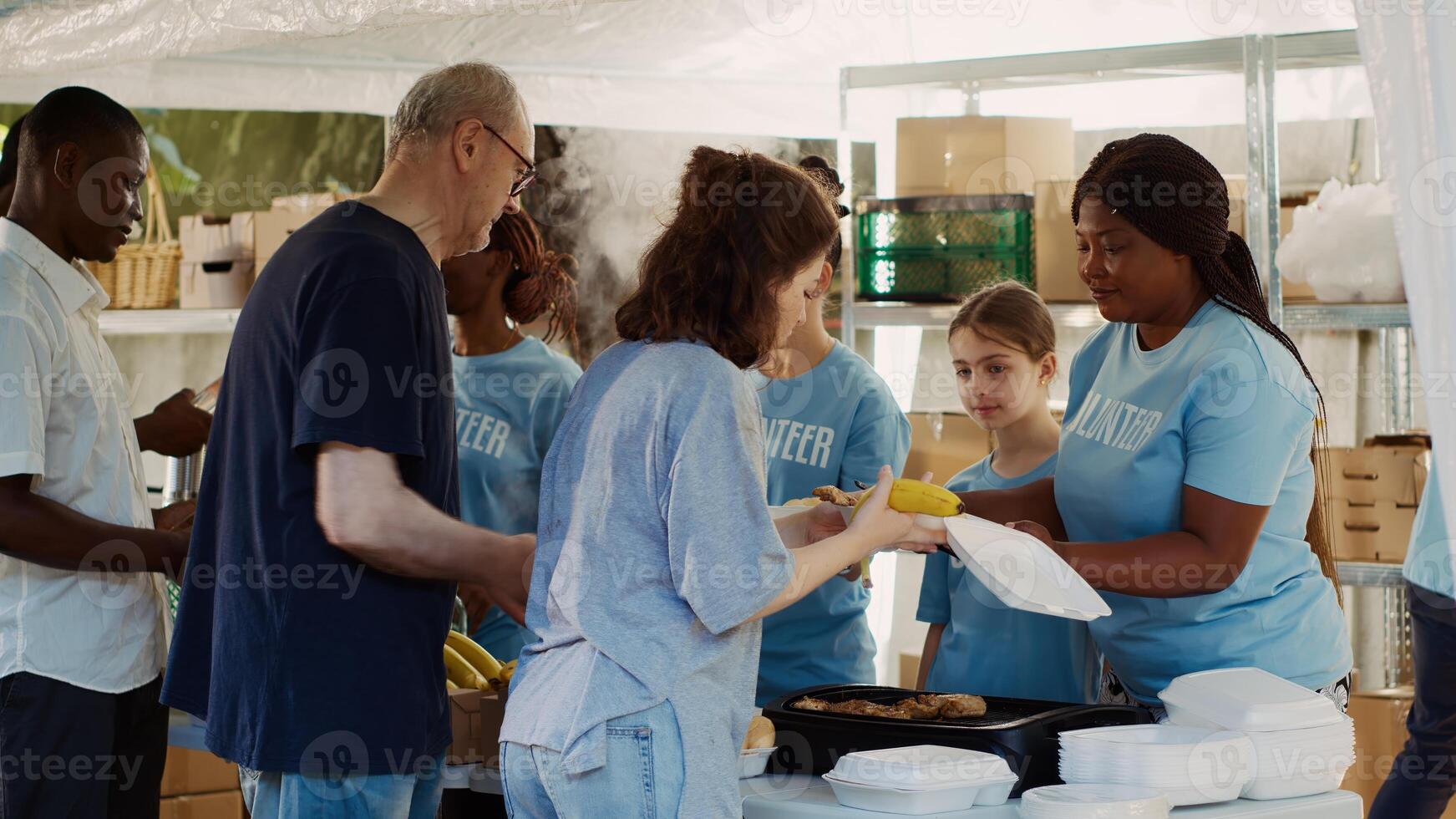 At a non-profit food drive event multicultural group of volunteers help the homeless and needy people. Friendly charity workers provide warm meals to the underprivileged. Tripod shot. photo