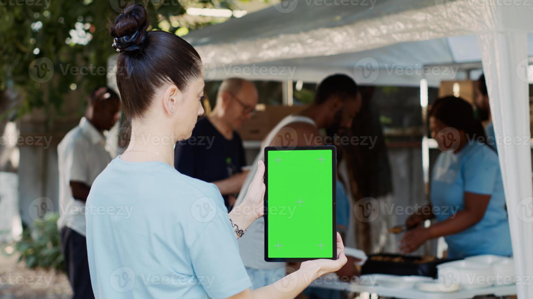 Caucasian lady holding smart tablet with a chromakey mockup template for customizable charity messages. Female volunteer vertically grasps a digital gadget with isolated green screen display. photo