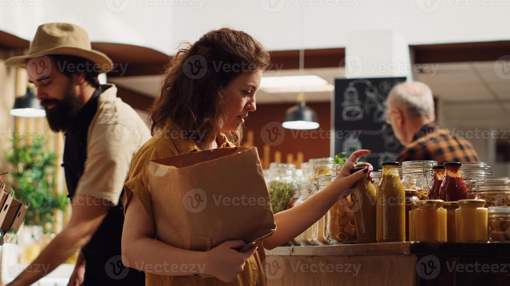 mujer agregando aditivos gratis natural despensa esenciales y vegetales en papel bolsa, consiguiendo producto recomendaciones desde vendedor en cero residuos supermercado. Al por menor empleado Ayudar cliente en tienda de comestibles tienda foto