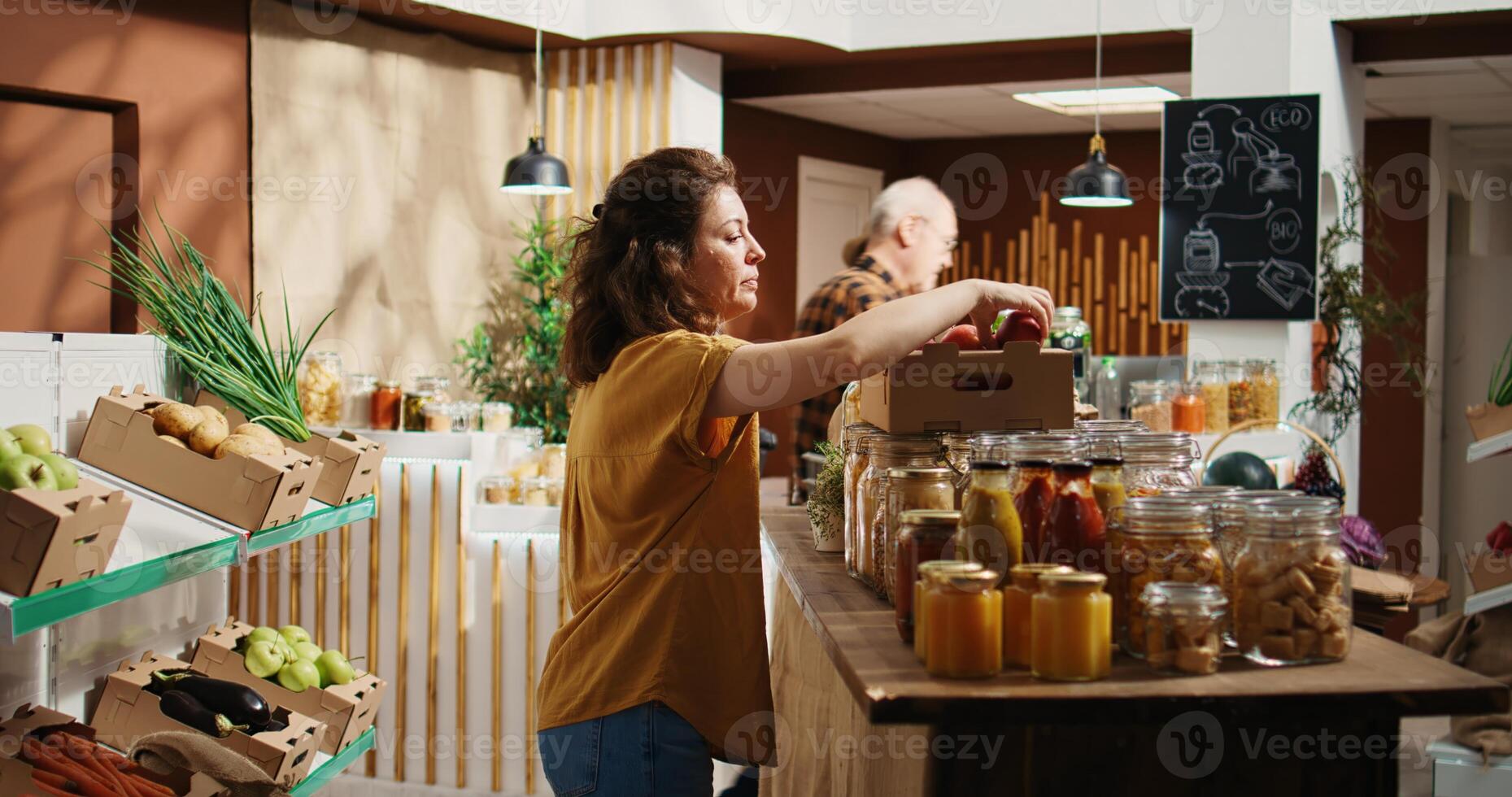 Woman in zero waste shop buying fruits, checking products before making purchase, ensuring they are pesticides free. Vegan client verifying apples in local bio food store are organic, smelling them photo